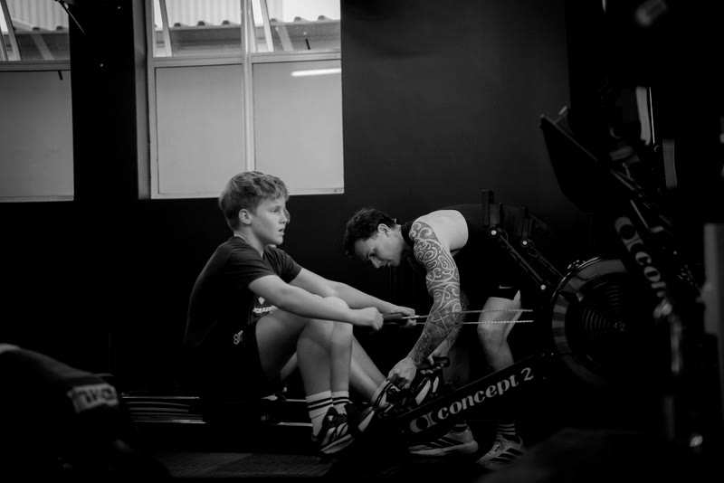 A coach guiding a young athlete on the rower