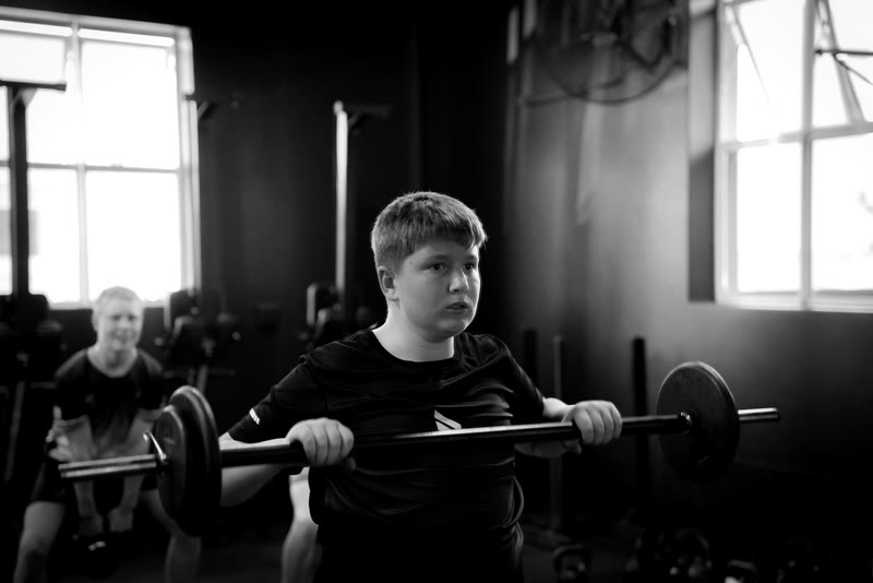 A young athlete lifting a barbell under supervision at Origin Fitness Studio